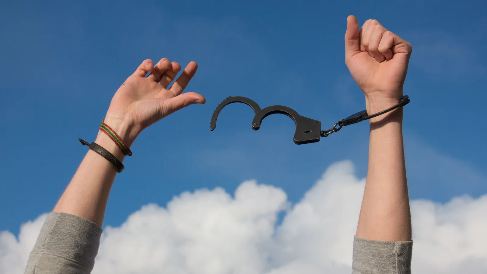 Unos brazos alzados contra un cielo azul liberándose de unas esposas abiertas, como metáfora de salir de deudas